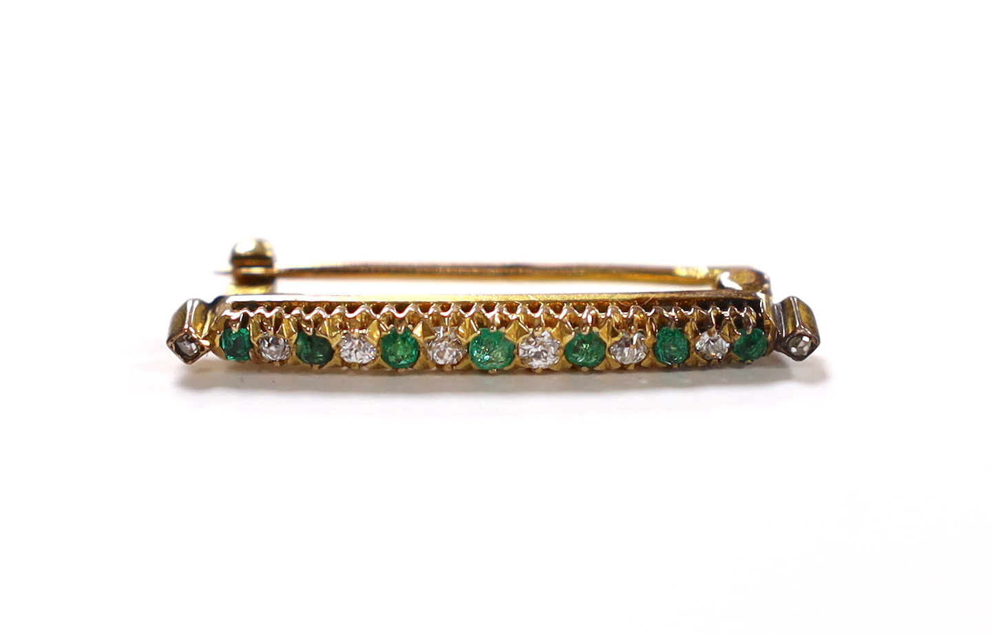 A yellow metal, seven stone emerald and eight stone diamond chip set bar brooch, 32mm, gross weight 2.9 grams.